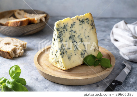 Blue cheese, dor blue or roquefort mold cheese slice on cutting board with basil leaves, lifestyle food. Blue cheese, dor blue or roquefort mold cheese slice on cutting board with basil leaves, lifestyle food. 89605383