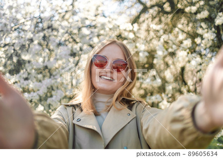 Close-up portrait of happy caucasian cheery young blond girl in red stylish sunglasses taking selfie in park at spring time 89605634