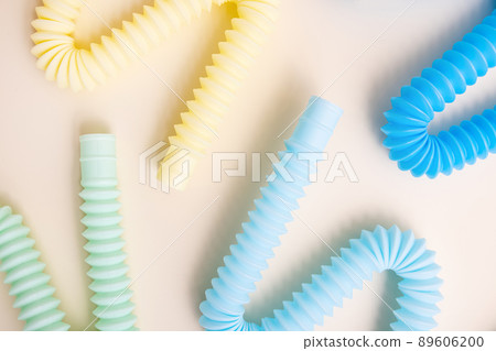 Trendy kids toys pastel colorful pop-tube on beige background. Set of forms and colors corrugated pipe and anti stressing, relaxation fidget finger toys.  89606200