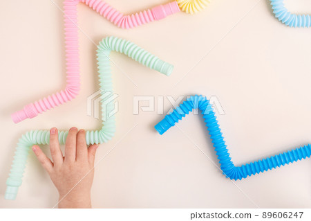 Trendy kids toys pastel colorful pop-tube in baby toddler hands on beige background. Set of forms and colors corrugated pipe and anti stressing, relaxation fidget finger toys. Trendy kids toys pastel colorful pop-tube in baby toddler hands on beige background. Set of forms and colors corrugated pipe and anti stressing, relaxation fidget finger toys. 89606247