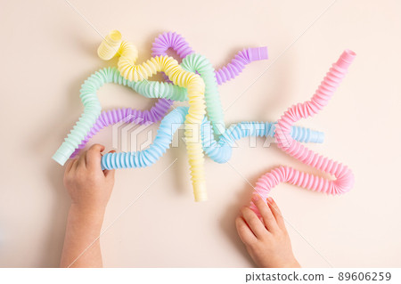 Trendy kids toys pastel colorful pop-tube in baby toddler hands on beige background. Set of forms and colors corrugated pipe and anti stressing, relaxation fidget finger toys. Trendy kids toys pastel colorful pop-tube in baby toddler hands on beige background. Set of forms and colors corrugated pipe and anti stressing, relaxation fidget finger toys. 89606259