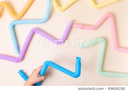 Trendy kids toys pastel colorful pop-tube in baby toddler hands on beige background. Set of forms and colors corrugated pipe and anti stressing, relaxation fidget finger toys.  89606288