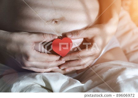 A pregnant woman after IVF holds a small red heart in her hands. The concept of motherhood, fertility, new life, In vitro fertilisation. Banner 89606972
