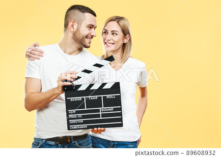 Young happy couple with cinema clapper board over yellow background 89608932