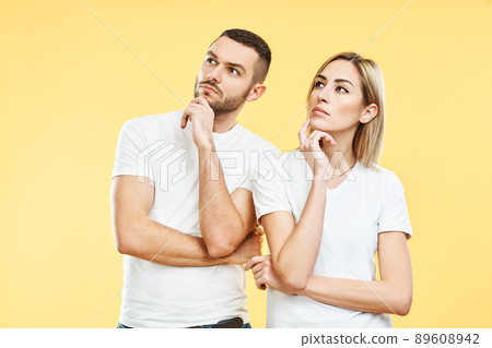 Young thoughtful man and woman looking sideways on yellow background. Young thoughtful man and woman looking sideways on yellow background. 89608942