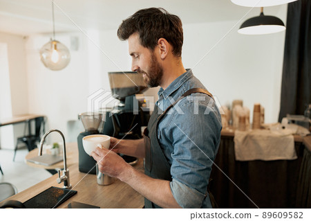 Handsome barista holding cup of coffee before giving to the client Handsome barista holding cup of coffee before giving to the client 89609582