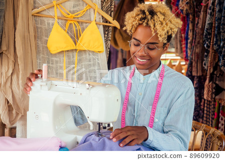 african american woman sewing a stylish yellow swimming suit for summer pool party in tropical workshop in Bali african american woman sewing a stylish yellow swimming suit for summer pool party in tropical workshop in Bali 89609920