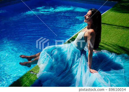 indian woman posing in blue long dress near swimming pool 89610034
