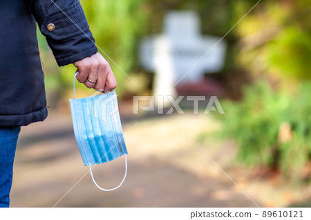 Woman, standing at the grave of family members with a facemask during the pandemic 89610121