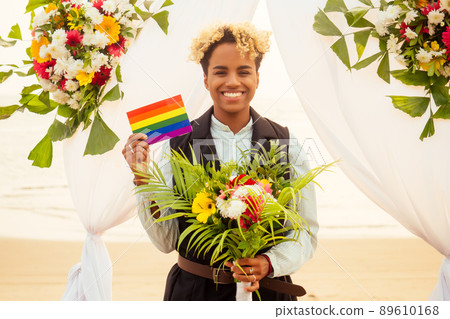 african american female groom in black suit and happy caucasian blonde bride loving together on beach ceremony under floral arch african american female groom in black suit and happy caucasian blonde bride loving together on beach ceremony under floral arch 89610168