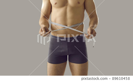 Sporty man who has been doing weight loss workouts is measuring his slim waistline Sporty man who has been doing weight loss workouts is measuring his slim waistline 89610458