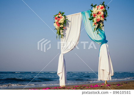 Beautiful summer wedding ceremony outdoors. Wedding arch made of light cloth and white and pink flowers on sea Beautiful summer wedding ceremony outdoors. Wedding arch made of light cloth and white and pink flowers on sea 89610581