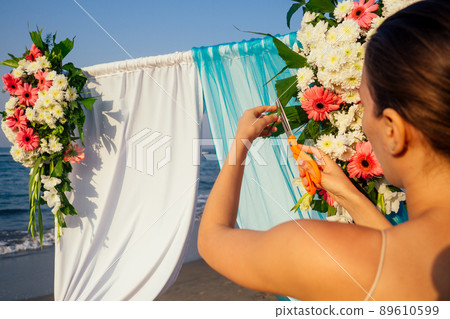 Decorator working with flowers composition for wedding arch on ocean beach 89610599