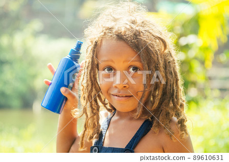 Mowgli indian boy with dreadlocks hair hiding holding mosquito spray in tropics green forest background Mowgli indian boy with dreadlocks hair hiding holding mosquito spray in tropics green forest background 89610631