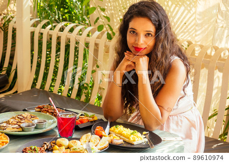 indian pretty woman in pink dress and curly hairstyle sitting in summer tropical cafe indian pretty woman in pink dress and curly hairstyle sitting in summer tropical cafe 89610974