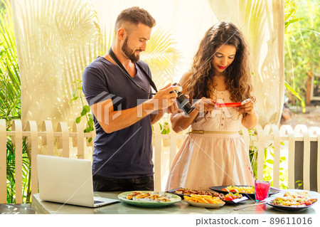 beautiful indian woman and arabian man photographing dishes in summer tropical cafe on camera 89611016