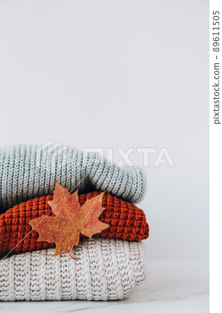 Stack of cozy knitted warm sweater with Autumn fall maple leaf. Sweaters in retro Style. Orange and blue colors. Cozy hygge concept Copy space 89611505