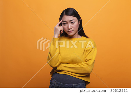 Serious pensive woman focused on introspection thoughts in a contemplation state on orange background. Concentrated young adult person in foreground standing and thinking about useful ideas. Serious pensive woman focused on introspection thoughts in a contemplation state on orange background. Concentrated young adult person in foreground standing and thinking about useful ideas. 89612311