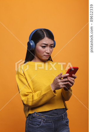 Doubtful uncertain young adult feeling confused because of smartphone acting weird. Confused clueless woman feeling helpless because of faulty smartphone device. Doubtful uncertain young adult feeling confused because of smartphone acting weird. Confused clueless woman feeling helpless because of faulty smartphone device. 89612339