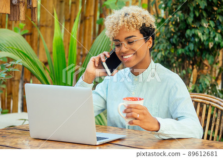 latin mixed race curly woman looking at laptop and smiling at tropical beach cafe with tea cup. She buying airline tickets online latin mixed race curly woman looking at laptop and smiling at tropical beach cafe with tea cup. She buying airline tickets online 89612681