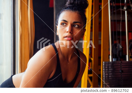 latin american fitness model in bra top and leggings looking tired with sweat on the forehead at dark gym latin american fitness model in bra top and leggings looking tired with sweat on the forehead at dark gym 89612702
