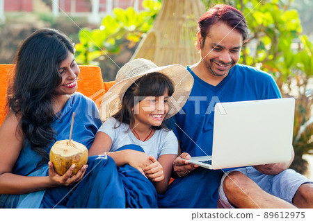 using eco metal recyclable tube.happy asian parents and cute girl enjoying summer vacation in Goa beach , drinking coconut water and looking at laptop videochat using eco metal recyclable tube.happy asian parents and cute girl enjoying summer vacation in Goa beach , drinking coconut water and looking at laptop videochat 89612975
