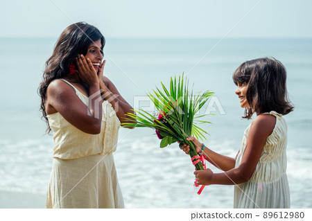Happy family with bouquet of flowers roses by the sea at sunset. Young beautiful amazed mother and daughter congratulating happy birthday.Valentine concept 89612980
