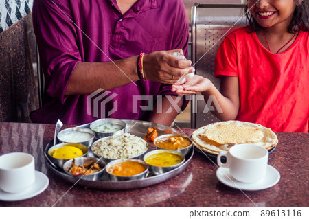 Father ,mother and little girl using wash hand sanitizer gel before eating in india cafe 89613116