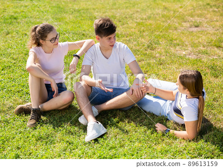 Cheerful teen boy and girls talking on green lawn Cheerful teen boy and girls talking on green lawn 89613159