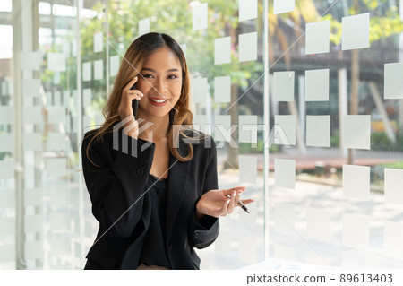 Portrait confident business asian woman calling on mobile phone at office window Portrait confident business asian woman calling on mobile phone at office window 89613403