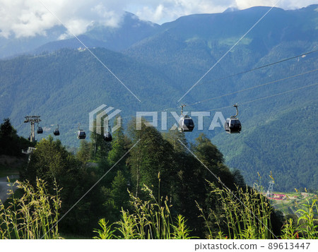 Cable way in Rosa Khutor (Russia). Lot of gondola cars moving along ropes, big mountain on horizon. Transportation on alpine resort. Sunny summer day. Cable way in Rosa Khutor (Russia). Lot of gondola cars moving along ropes, big mountain on horizon. Transportation on alpine resort. Sunny summer day. 89613447