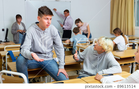 Girl and boy are sitting at the desk and talking about life in classroom. Girl and boy are sitting at the desk and talking about life in classroom. 89613514