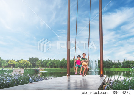 Two asian siblings is swinging on a giant swing in a public park with blue sky. Two asian siblings is swinging on a giant swing in a public park with blue sky. 89614222