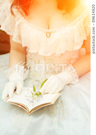 Cleavage of a woman in a beautiful blue dress, she is holding a book open and a flower. High quality photo Cleavage of a woman in a beautiful blue dress, she is holding a book open and a flower. High quality photo 89614920