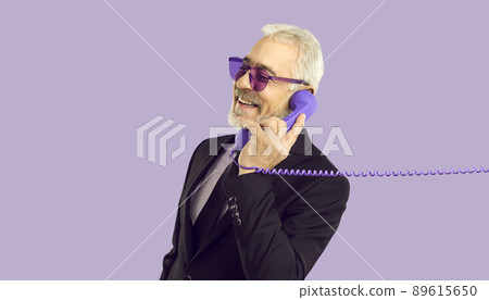 Cheerful stylish and charismatic senior man talking on landline phone on purple background. 89615650