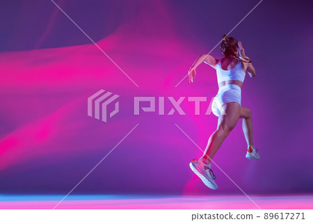 back view. Professional female athlete, runner training isolated on blue studio background in mixed pink neon light. back view. Professional female athlete, runner training isolated on blue studio background in mixed pink neon light. 89617271