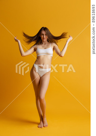 Beautiful woman with slim figure posing in white underwear isolated over yellow studio background 89618693