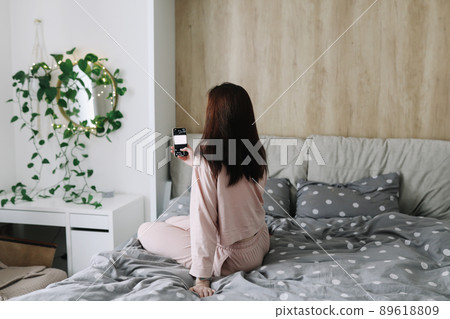 Pretty young woman sitting in bed and makes selfie Pretty young woman sitting in bed and makes selfie 89618809