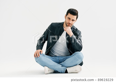 Handsome trendy man sitting on floor isolated on white studio background Handsome trendy man sitting on floor isolated on white studio background 89619229
