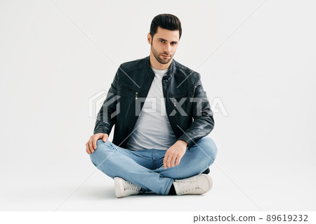 Handsome trendy man sitting on floor isolated on white studio background Handsome trendy man sitting on floor isolated on white studio background 89619232