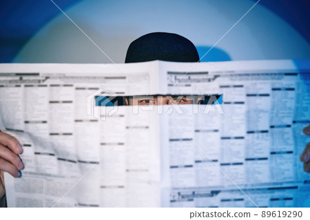 Man hiding watches through the newspaper in the spotlight on studio background 89619290