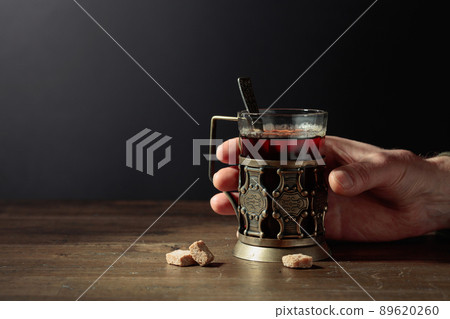 Man hand holds a traditional Russian glass holder with hot tea. Man hand holds a traditional Russian glass holder with hot tea. 89620260