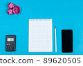 Office table desk with tablet, smartphone, calculator, flowers and blank notepad on blue. Top view copy space text 89620505