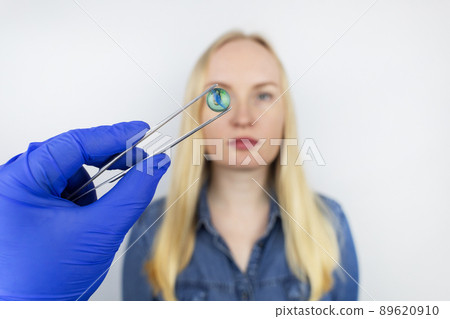 Conceptual shot of an eye crystalline lens replacement. Ophthalmic surgery. Return of sight. Removal of cataracts. Surgical intervention in the eyeball. Doctor holds the implant near the patient Conceptual shot of an eye crystalline lens replacement. Ophthalmic surgery. Return of sight. Removal of cataracts. Surgical intervention in the eyeball. Doctor holds the implant near the patient 89620910