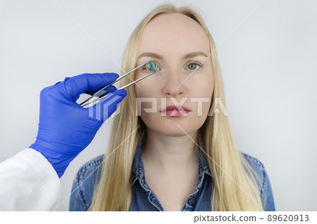 Conceptual shot of an eye crystalline lens replacement. Ophthalmic surgery. Return of sight. Removal of cataracts. Surgical intervention in the eyeball. Doctor holds the implant near the patient Conceptual shot of an eye crystalline lens replacement. Ophthalmic surgery. Return of sight. Removal of cataracts. Surgical intervention in the eyeball. Doctor holds the implant near the patient 89620913