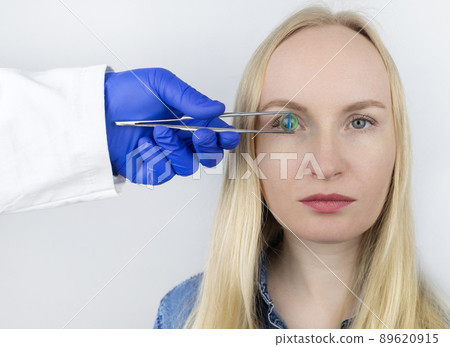 Conceptual shot of an eye crystalline lens replacement. Ophthalmic surgery. Return of sight. Removal of cataracts. Surgical intervention in the eyeball. Doctor holds the implant near the patient Conceptual shot of an eye crystalline lens replacement. Ophthalmic surgery. Return of sight. Removal of cataracts. Surgical intervention in the eyeball. Doctor holds the implant near the patient 89620915