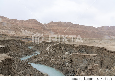 Sinkhole filled with turquoise water, near Dead Sea coastline. Hole formed when underground salt is dissolved by freshwater intrusion, due to continuing sea-level drop.  89621703
