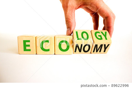 Ecology or economy symbol. Businessman turns wooden cubes and changes the concept word Economy to Ecology. Beautiful white table white background. Business ecology or economy concept. Copy space. Ecology or economy symbol. Businessman turns wooden cubes and changes the concept word Economy to Ecology. Beautiful white table white background. Business ecology or economy concept. Copy space. 89622996