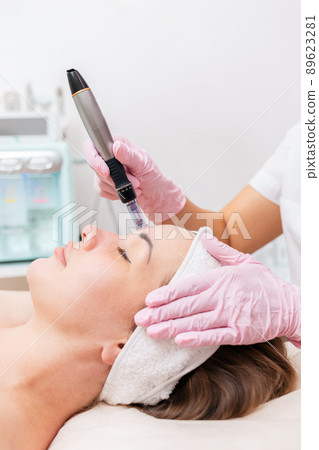 Beauty salon. Cosmetologist in rubber gloves makes fractional mesotherapy of the face to the client. Side view. Face close up. Concept of professional cosmetology and beauty Beauty salon. Cosmetologist in rubber gloves makes fractional mesotherapy of the face to the client. Side view. Face close up. Concept of professional cosmetology and beauty 89623281