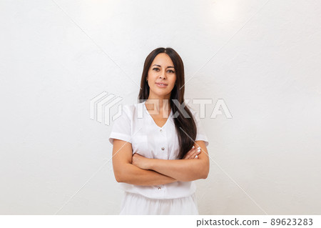 A tanned, pretty woman smiles and poses with her arms crossed. White background. Copy space. Concept of advertising business, and expressions 89623283